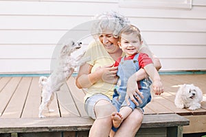 Grandmother sitting with grandson boy on porch at home backyard. Bonding of relatives and generation communication. Old woman with