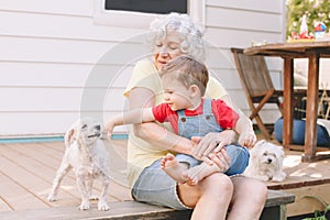 Grandmother sitting with grandson boy on porch at home backyard. Bonding of relatives and generation communication. Old woman with