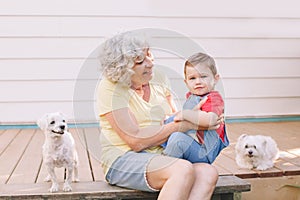 Grandmother sitting with grandson boy on porch at home backyard. Bonding of relatives and generation communication. Old woman with