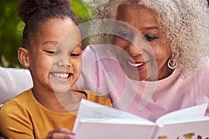 Grandmother Sitting Outdoors With Granddaughter At Home Reading Book Together