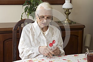 Grandmother sitting at a table in the living room and lubricates hand salve.