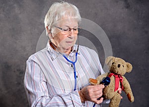 Grandmother with stethoscope is puppet doctor for teddy bear