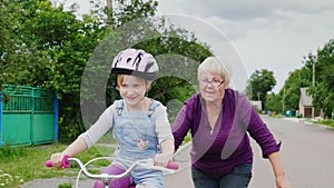 Grandmother teaches her granddaughter how to ride a bicycle. The first successes of children, activity in old age