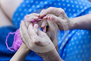 Grandmother teaches her granddaughter to knit. Hands of old woman and young girl. Shallow DOF.