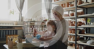 Grandmother teaches her granddaughter working on a pottery rotating wheel