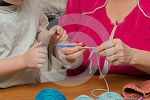 Grandmother teaches her grandson to crochet. Close-up of hands of grandmother and child. Horizontal photo. Concept - training,