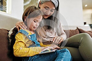 Grandmother teaching granddaughter to use tablet at home