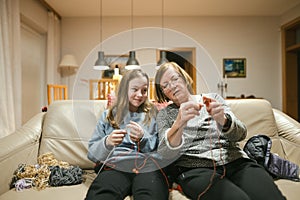 Grandmother and teenage granddaughter knitting on a sofa. Grandma teaching teen child to knit