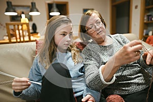 Grandmother and teenage granddaughter knitting on a sofa. Grandma teaching teen child to knit