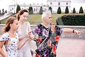 Grandmother and two granddaughters are walking around the city on the street. Walk around the city with your beloved grandmother.