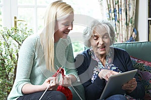 Grandmother Using Digital Tablet As Granddaughter Knits