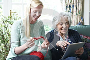 Grandmother Using Digital Tablet Whilst Granddaughter Knits