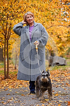 Grandmother walks with a dog in an autumn park straightens her hair