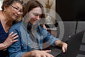 A grandmother who is hugging her teenage grandson while he is using the laptop.