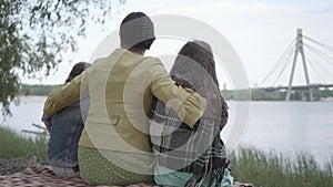 Grandmother who sitting with two granddaughters in the banch and looking at beautiful river in the forest. Lady hug her