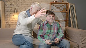 Grandpa enjoys the victory of his grandson in the console game. The old man is sitting on the couch with a young fat boy