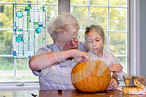 Grandpa and grand daughter scoop out the insides of a pumpkin