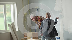 Grandpa and grandson is carrying heavy cardboard box and placing it on floor by window. Elderly man cries out in pain in