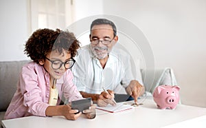 Grandpa and Grandson Engaging in Finance Education Calculating Savings Indoor