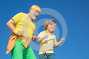 Grandpa and grandson exercising on blue sky. Cheerful grandpa and cute child grandson jogging in sportswear on sky