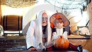 Grandpa and grandson with pumpkin together as preparation for Halloween. Cheerful children in Halloween costumes and