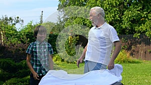 Grandpa and grandson spreading white table cloth, giving high five to each other