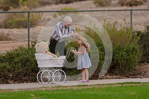 Grandpa helping little girl with hat on walk with toy buggy