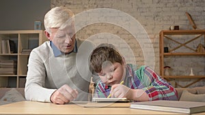 Grandpa helps a grandson with homework. Elderly man helps a young fat child to do homework. Home comfort, family idyll