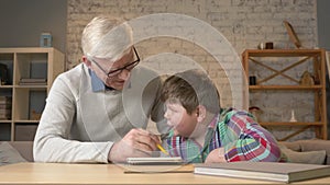 Grandpa helps a grandson with homework. Elderly man helps a young fat child to do homework. Home comfort, family idyll