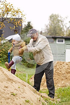 Grandpa helps grandson to get on a sand hill