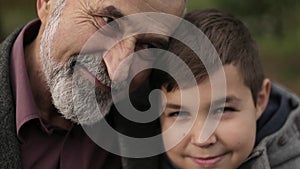 Grandpa and his grandson spend time together in the park. They are sitting on the bench