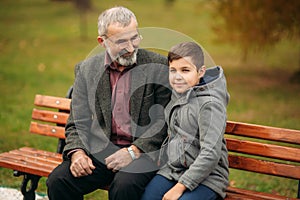 Grandpa and his grandson spend time together in the park. They are sitting on the bench