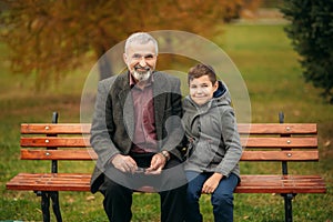 Grandpa and his grandson spend time together in the park. They are sitting on the bench