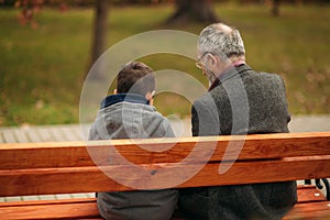 Grandpa and his grandson spend time together in the park. They are sitting on the bench. Walking in the park and