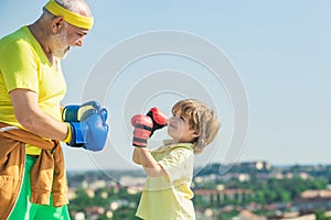 Grandpa and little child boy in boxing stance doing exercises with boxing gloves. Elderly man hitting punching bag