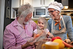 Grandpa persuading his granddaughter to eat carrot. grandma watching and laughing photo