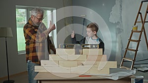 Grandpa shows his grandson how the water level installed on a brick wall works. Elderly man and young guy show thumbs up