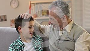 Grandpa stroking grandson head, hugging and looking at camera, family time