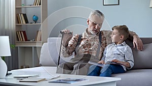 Grandpa watching photo album with grandson, recalling stories from happy youth