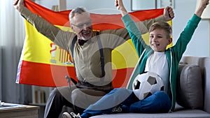 Grandpa waving Spanish flag, together with boy rejoices victory of football team