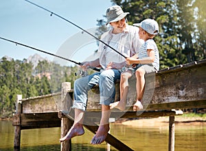 Grandpa will teach him all he needs to know. Shot of a little boy fishing with his grandfather at a lake in a forest.