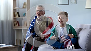 Grandpa wrapped in American flag watching sport with boy, worrying about game