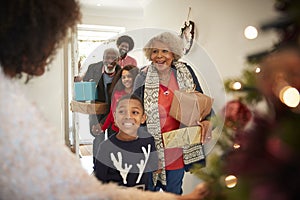 Grandparents Being Greeted By Family As They Arrive For Visit On Christmas Day With Gifts