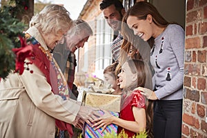 Grandparents Being Greeted By Family As They Arrive For Visit On Christmas Day With Gifts