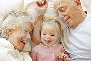 Grandparents Cuddling Granddaughter In Bed photo