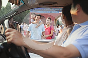 Grandparents driving and sitting in car and saying good bay to grandson and parents, view through window of car