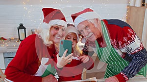 Grandparents family with granddaughter kid taking selfie photo on mobile phone at Christmas kitchen