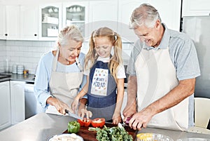 Grandparents, girl child in kitchen and cooking healthy food with vegetables on cutting board for happy family lunch at