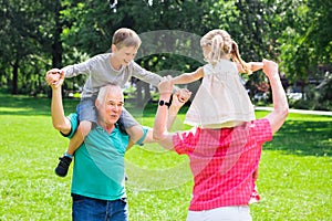 Grandparents Giving Grandchildren Piggyback Ride In Park