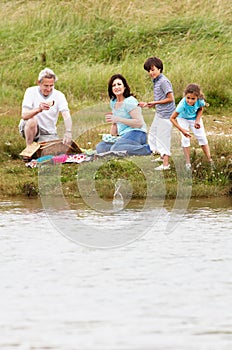 Grandparents And Grandchildren Having Picnic On Riverbank